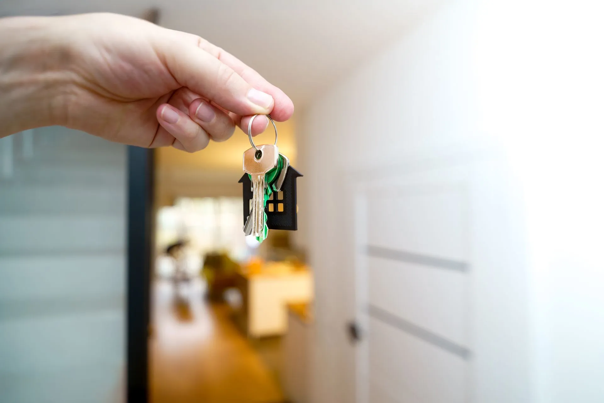  A person’s hand displaying a key, with a house visible behind, illustrating the idea of unlocking a new home.